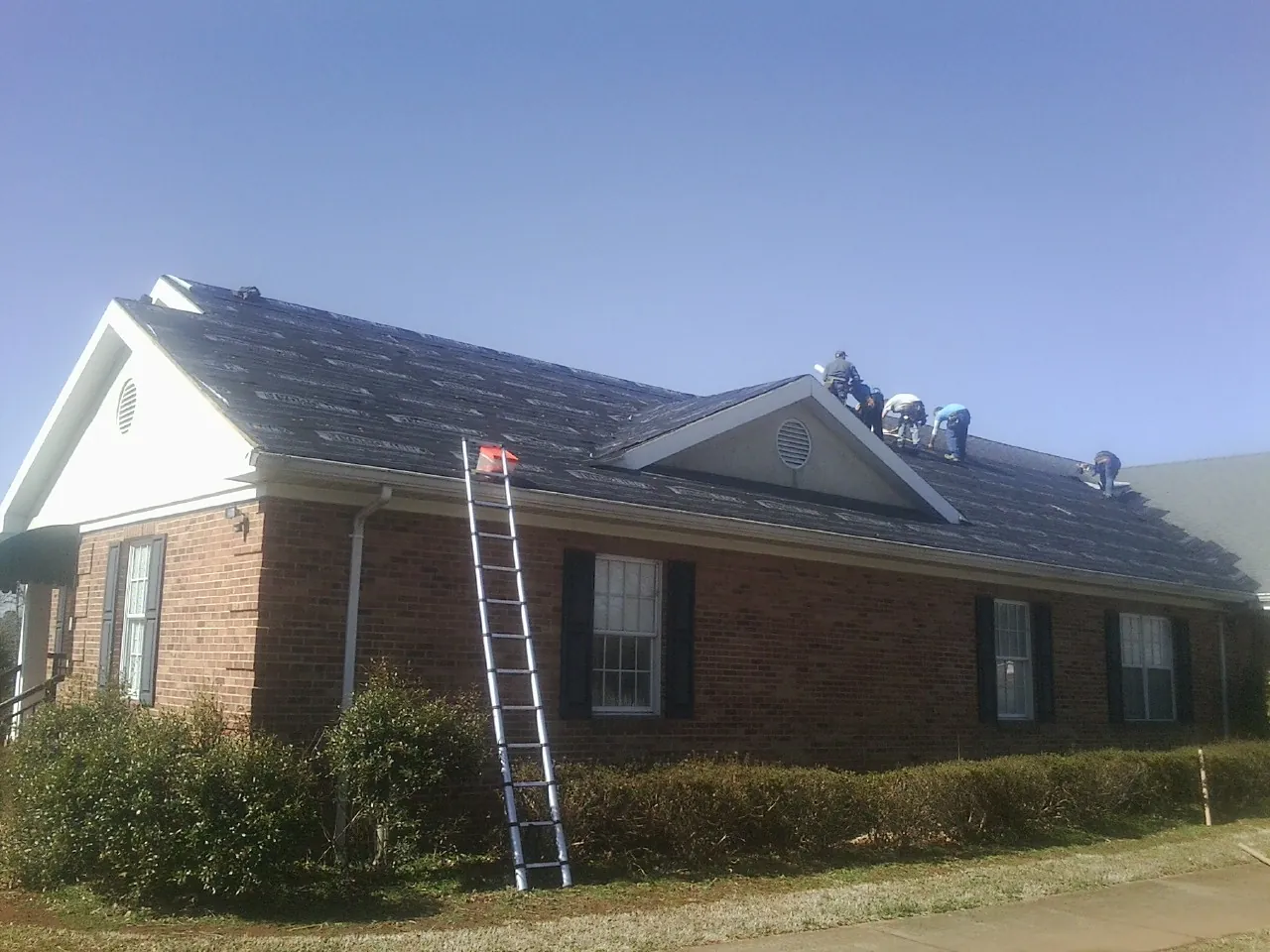 Crew tearing shingles off a brick ranch roof with a ladder set — Metal Roof Repair work by our crew in Wartrace
