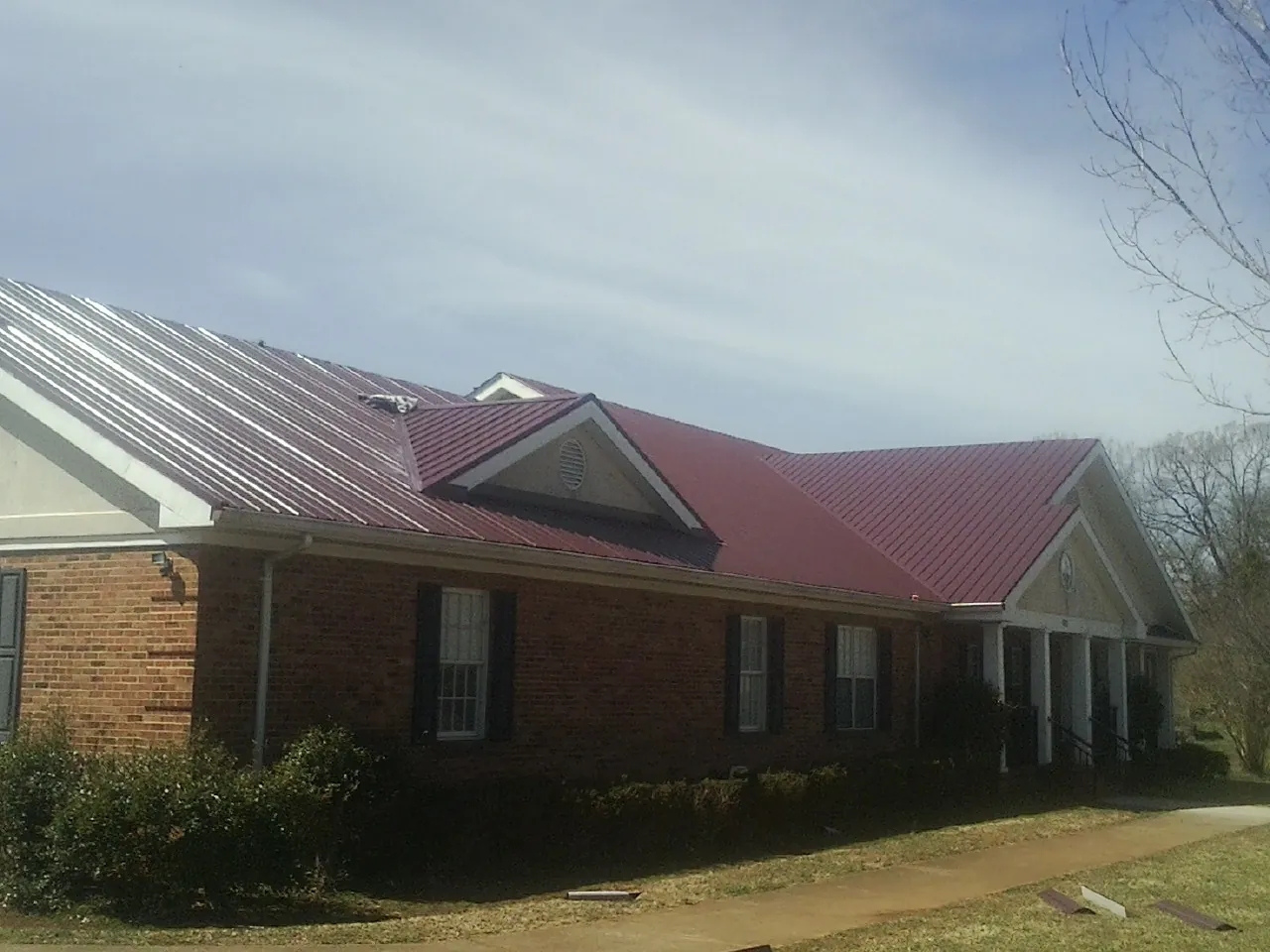 Red metal roof with gabled entries on a long brick building, from a Hail Damage Roof Repair job in Wartrace