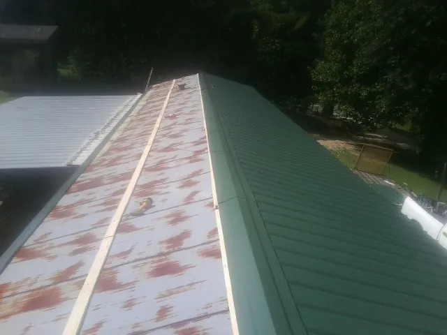 Old rusted panels beside newly installed green metal roofing — Wind Damage Roof Repair by Roofing Brothers in Wartrace