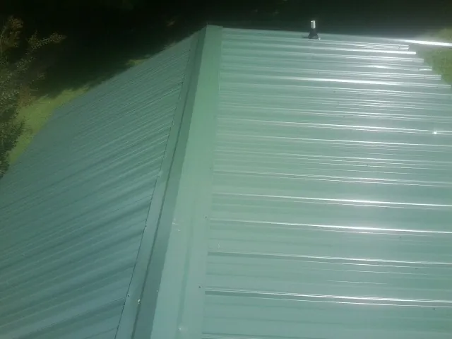 New green metal panels meeting at the ridge of a roof — Flat Roof Repair work by our crew in Wartrace