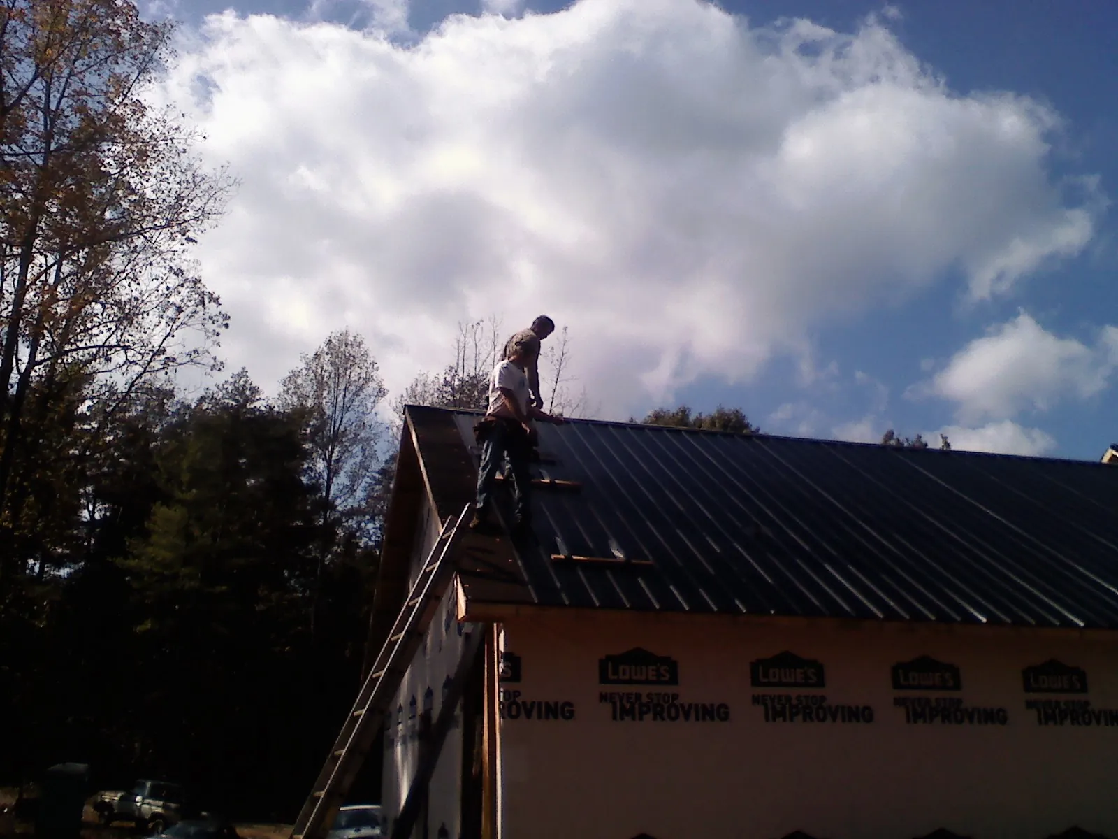 Roofer fastening dark metal panels high against a cloudy sky, from a Roof Inspection job in Wartrace