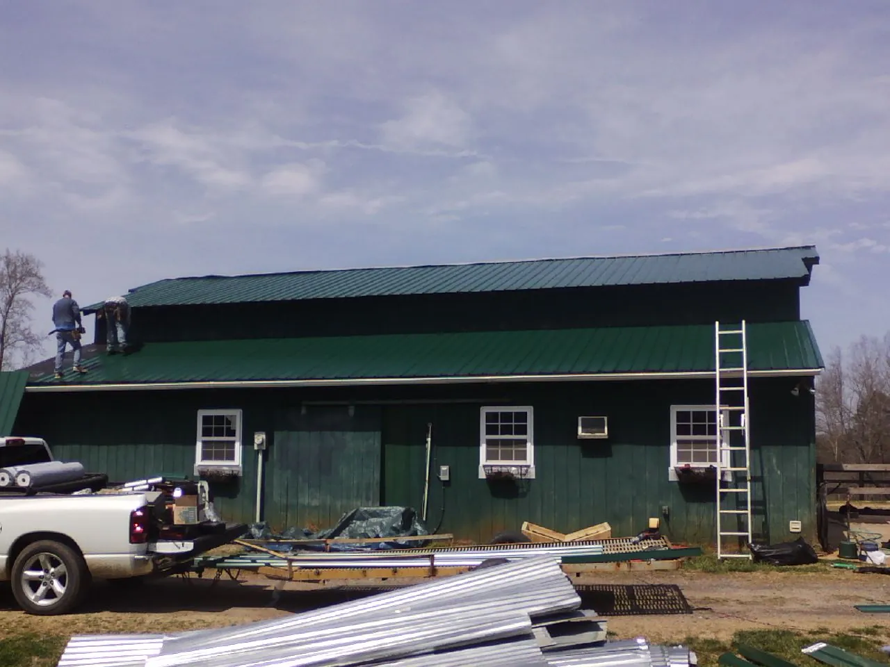 Crew installing green metal roofing on a large green barn in Wartrace