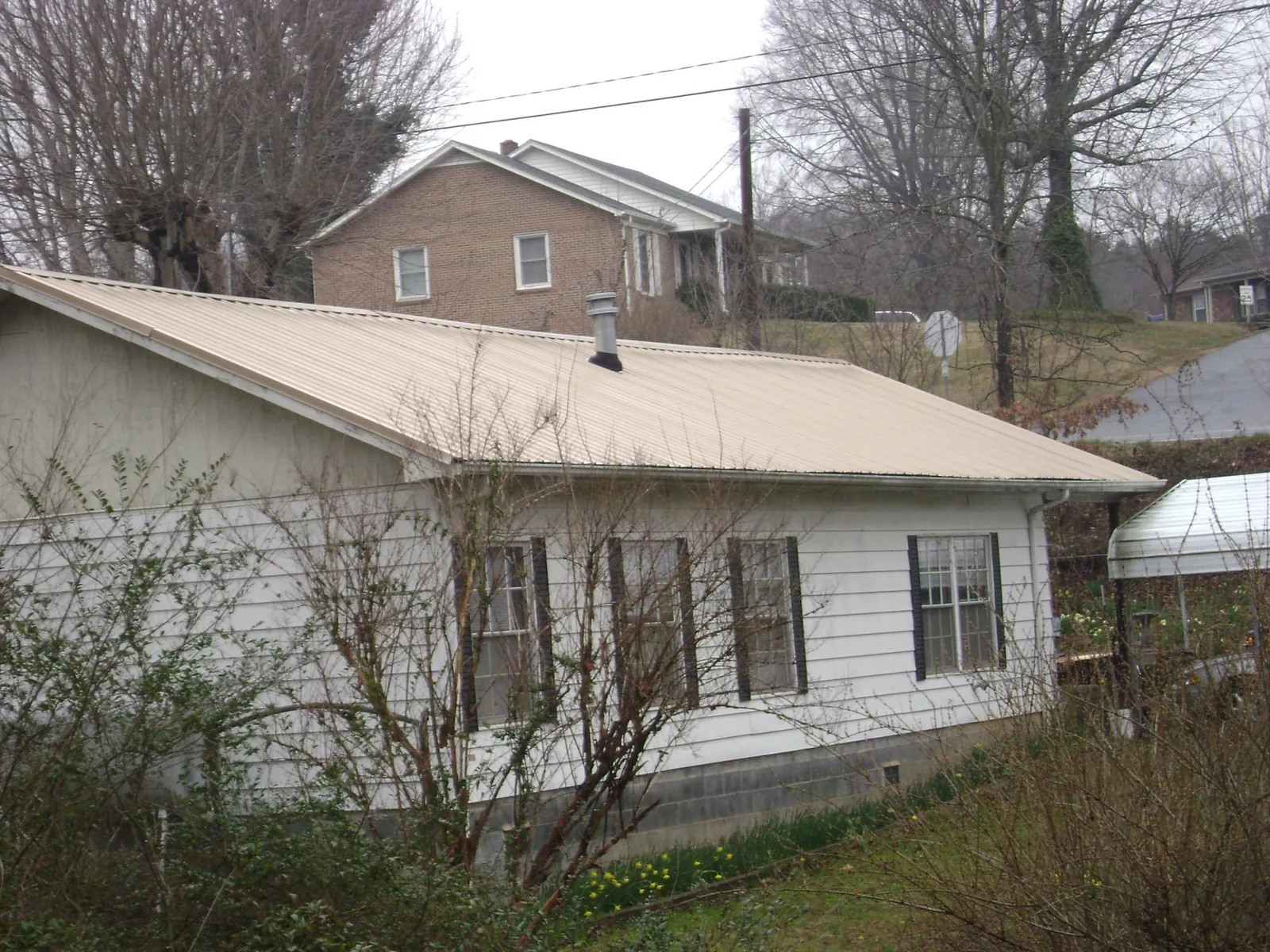 Tan metal roof on a white sided house set into a hillside — Commercial Roofing by Roofing Brothers in Wartrace